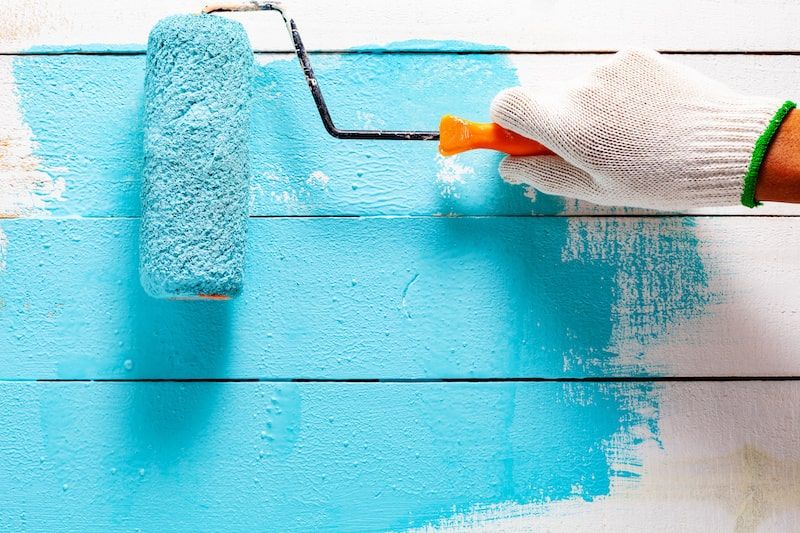 roller being used to paint a wooden bench blue