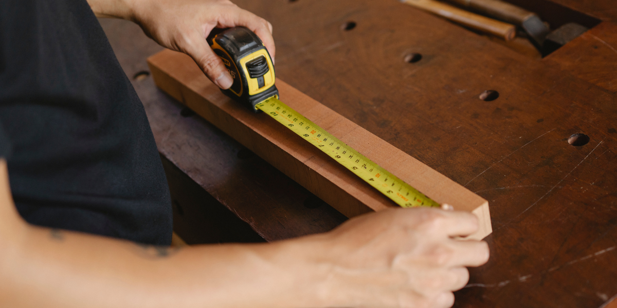 a person measuring a block of wood with a tape measure