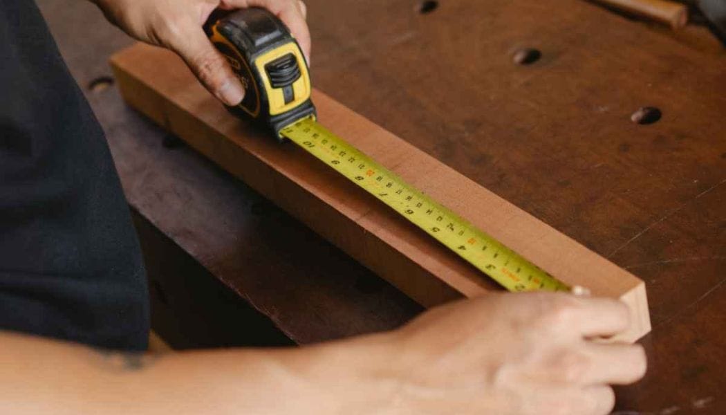 a person measuring a block of wood with a tape measure