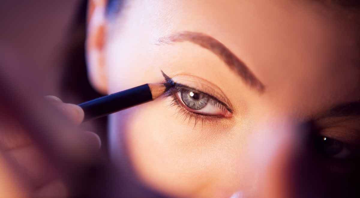 A girl applying eyeliner with a pencil liner