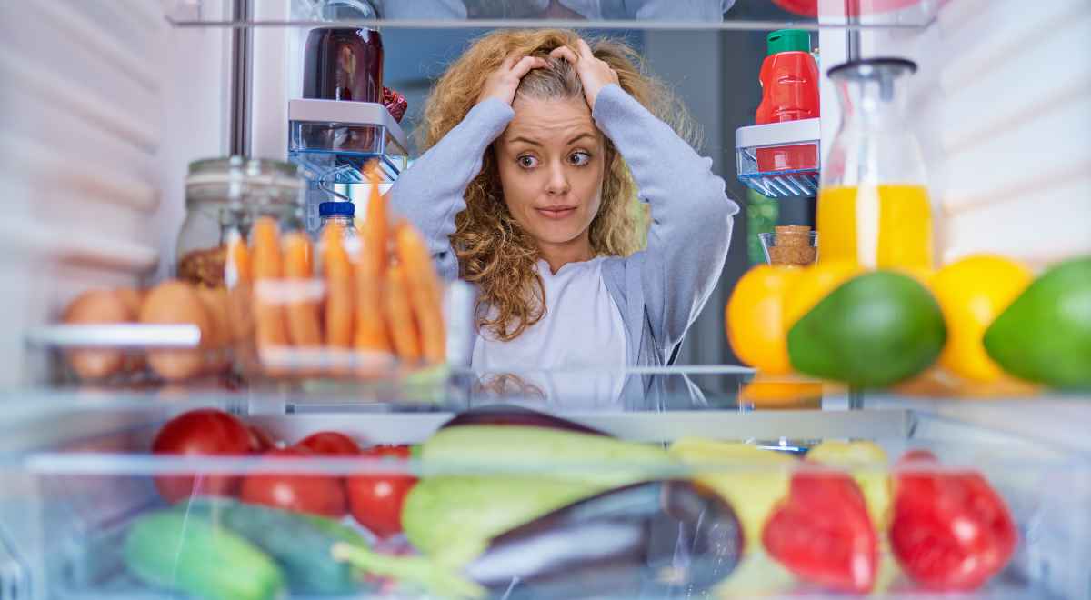 A girl with her hands over her head looking inside the fridge