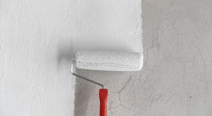 Painting a wall with a roller dipped in white paint