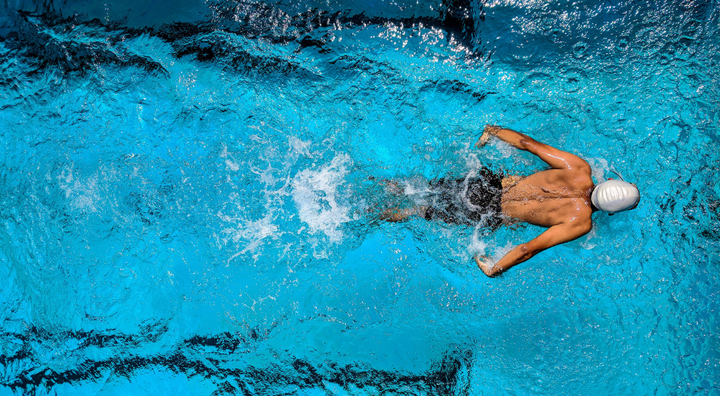 Man swimming in a swimming pool with a white swim cap