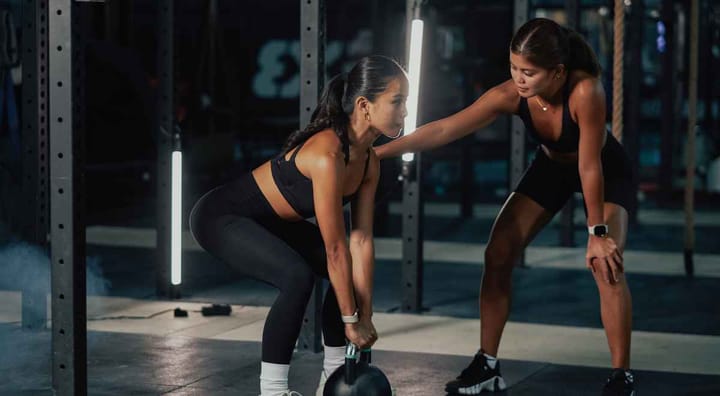 Fitness trainer assisting a woman lift a kettlebell