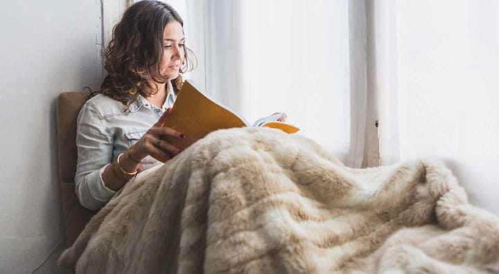 a girl reading a book by window with her blanket