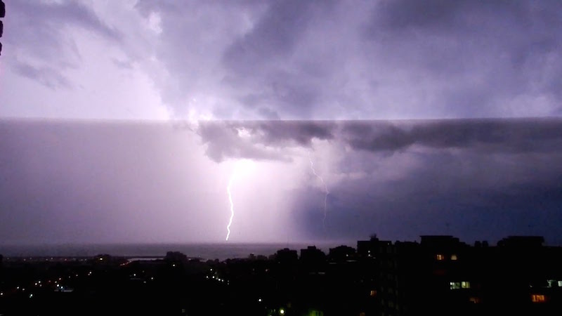 lightining flash in a purple sky at night over a city in the rainy season