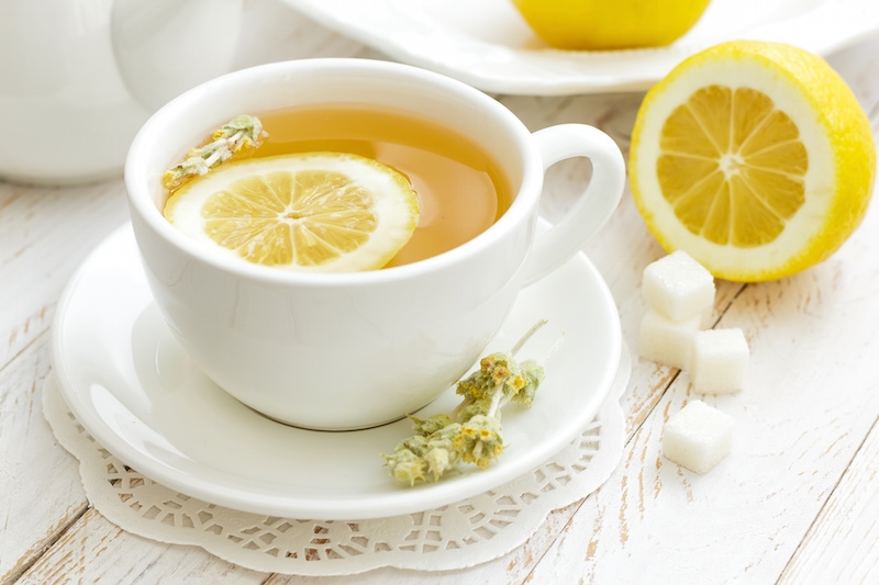 white cup of tea with a slice of lemon in it and more lemon and sugar on the table beside it 