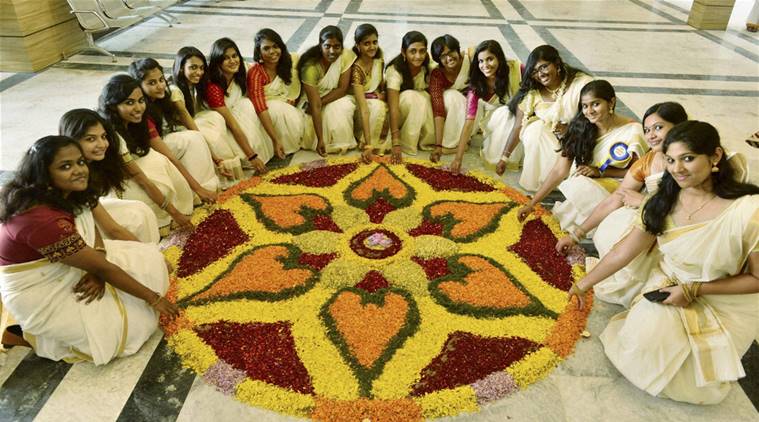 girls in white sarees sitting around a traditional onam rangoli