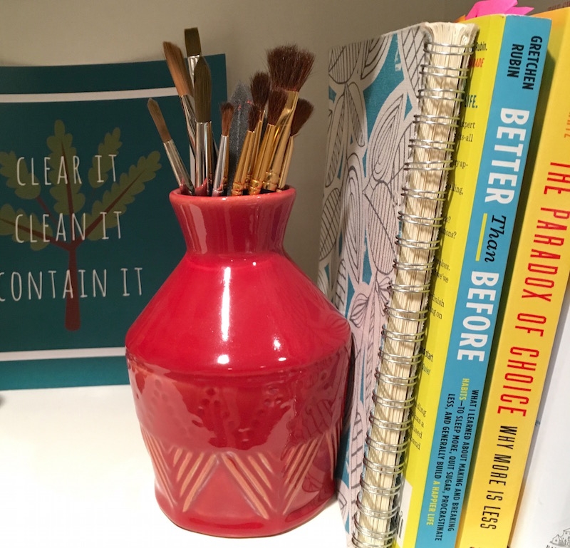 paintbrushes in a pot beside books